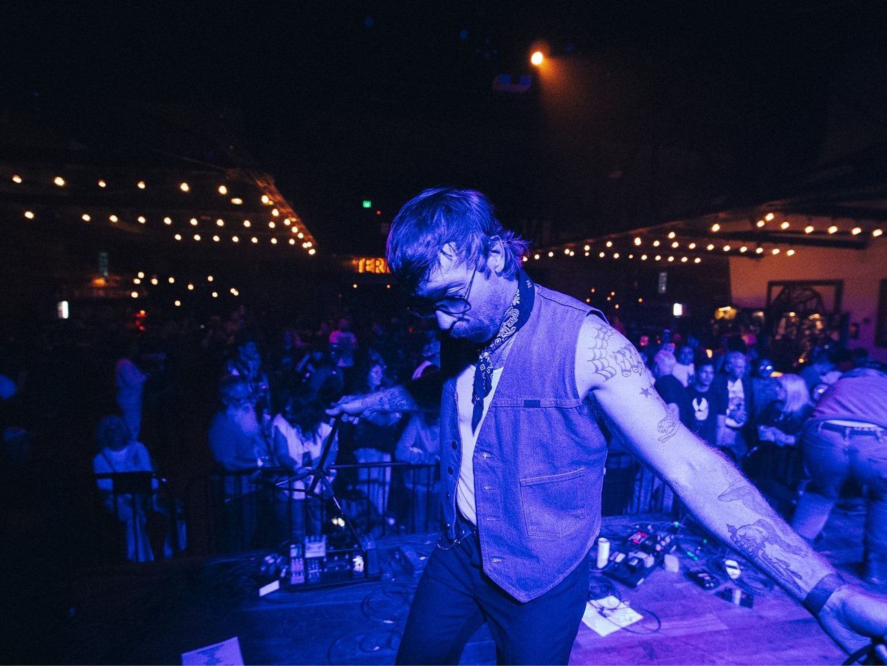 Trappers Pass on stage in a denim vest in front of a crowd under string lights